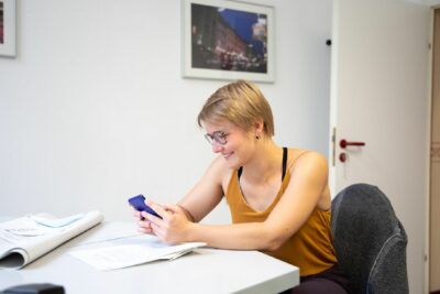 Evelyn Linde sitzt am Schreibtisch und blickt auf ihr Smartphone.